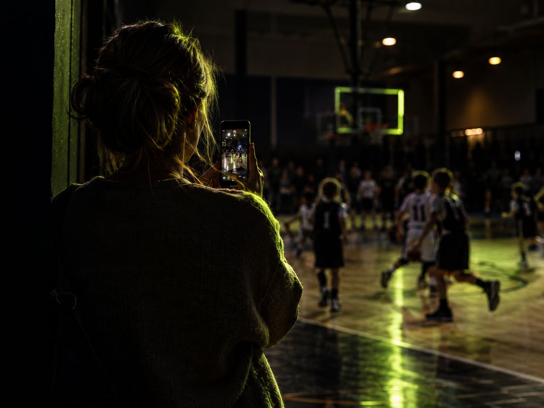 A parent watching a youth basketball game from the sideline